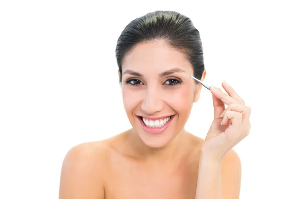 Brunette plucking her eyebrows and smiling at camera — Stock Photo, Image