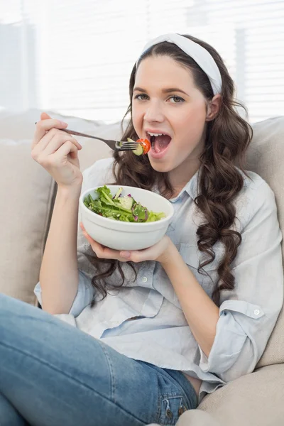 Carino donna casual sul divano accogliente mangiare insalata — Foto Stock