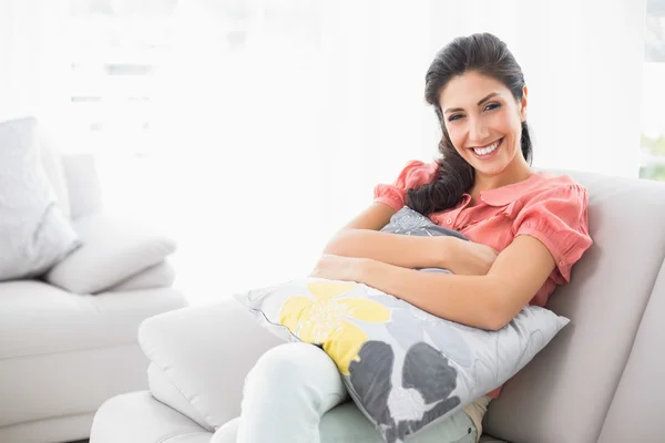 Glückliche Brünette sitzt auf ihrem Sofa und lächelt in die Kamera — Stockfoto