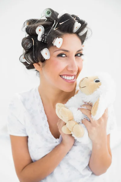 Happy brunette in hair rollers holding sheep teddy — Stock Photo, Image