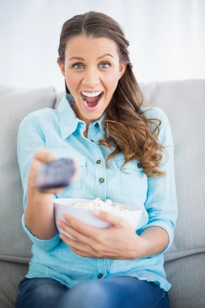 Surprised woman sitting on sofa changing tv channel — Stock Photo, Image