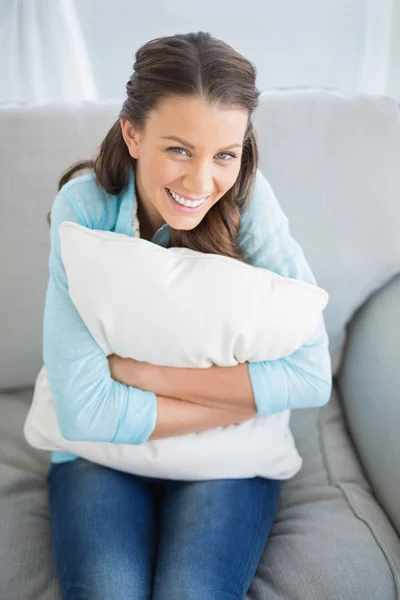 Mujer feliz sosteniendo almohada sentada en el sofá —  Fotos de Stock