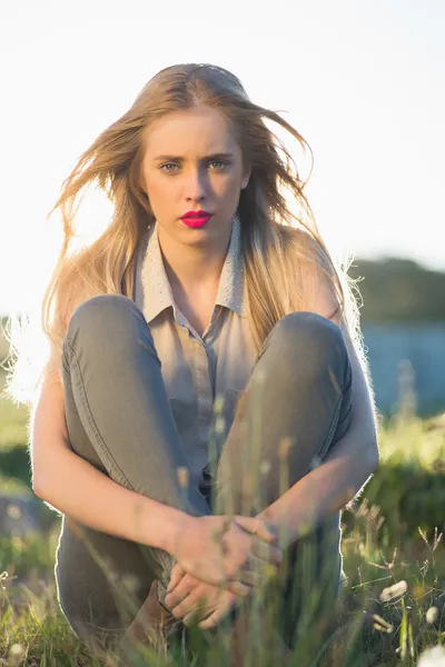 Blonde woman with red lips sitting in grass — Stock Photo, Image