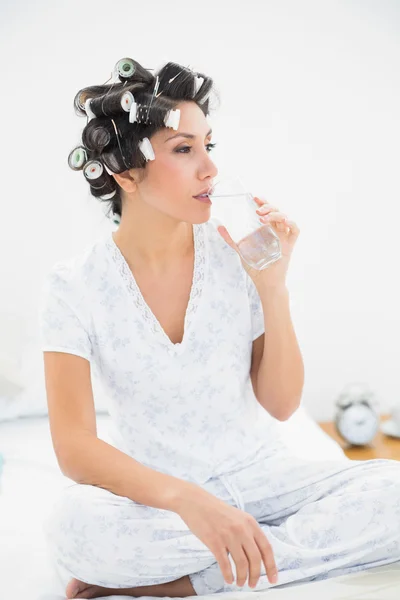 Mooie brunette in haar rollen glas water te drinken — Stockfoto