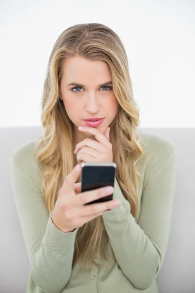 Thoughtful pretty blonde sending a text sitting on cosy sofa — Stock Photo, Image