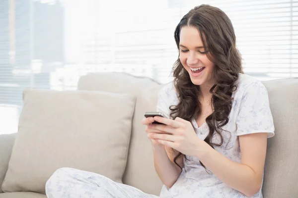 Χαμογελώντας όμορφη γυναίκα πιτζάμες ανάγνωση ένα κείμενο στο smartphone σε — Φωτογραφία Αρχείου