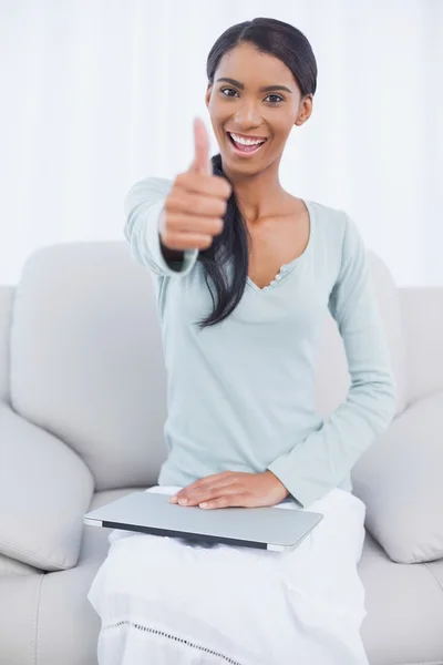 Cheerful attractive woman sitting on cosy sofa giving thumbs up — Stock Photo, Image