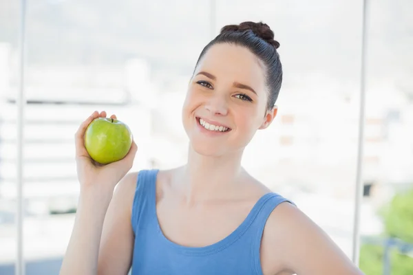 Cheerful slender woman in sportswear holding green apple — Stock Photo, Image