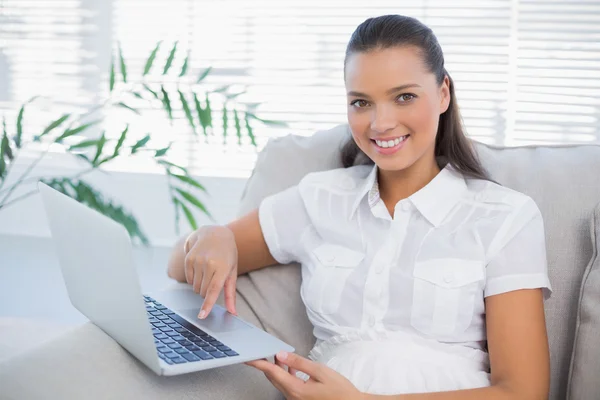 Smiling pretty woman using laptop sitting on cosy sofa — Stock Photo, Image