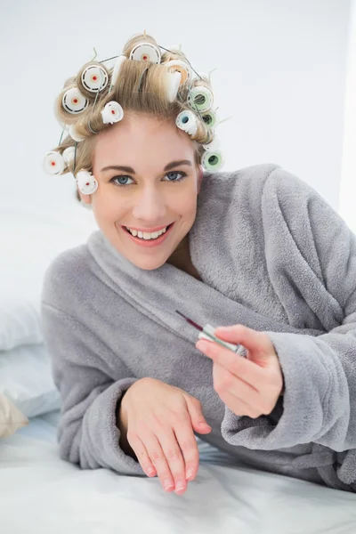 Cheerful relaxed blonde woman in hair curlers applying nail polish — Stock Photo, Image