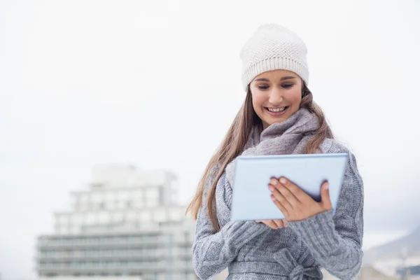 Smiling woman with winter clothes on using her tablet — Stock Photo, Image