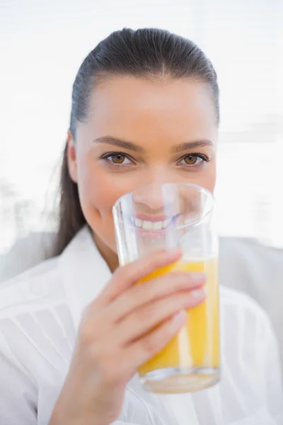 Mooie vrouw drinken sinaasappelsap zittend op gezellige Bank glimlachen — Stockfoto