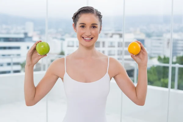 Cheerful sporty brunette holding apple and orange — Stock Photo, Image