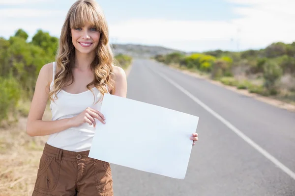 Smiling pretty woman holding sign while hitchhiking — Stock Photo, Image
