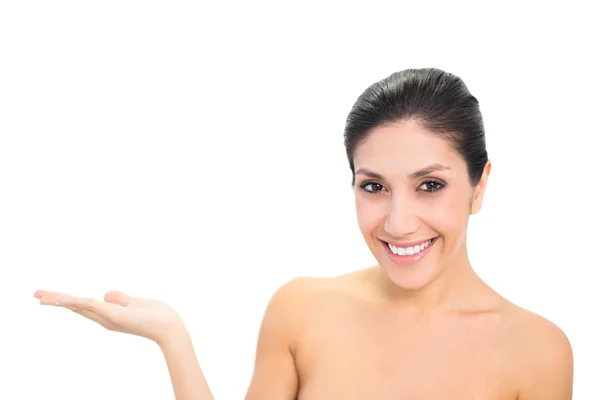 Smiling brunette presenting with hand looking at camera — Stock Photo, Image