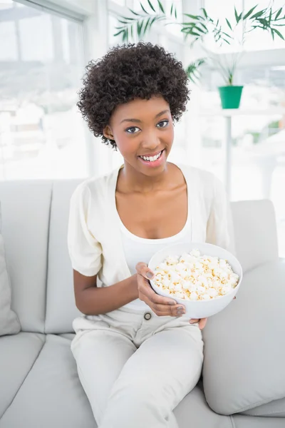 Atractiva morena sosteniendo palomitas de maíz sentada en un acogedor sofá —  Fotos de Stock