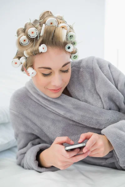 Sonriente mujer rubia relajada en rulos de pelo usando su teléfono móvil —  Fotos de Stock