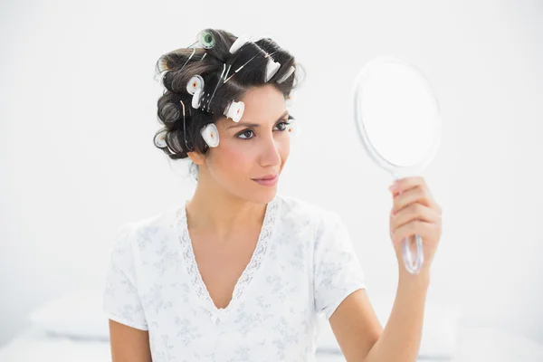 Happy brunette in hair rollers holding hand mirror — Stock Photo, Image