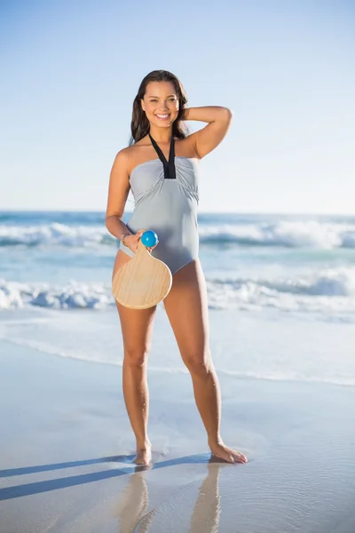Donna felice in costume intero in posa con racchetta da spiaggia — Foto Stock