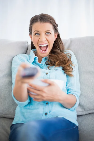 Mujer sentada en el sofá gritando mientras ve la televisión —  Fotos de Stock