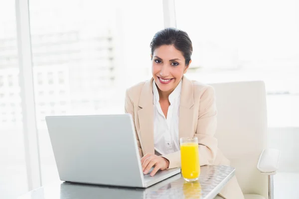 Glad affärskvinna med laptop och glas apelsinjuice på skrivbord — Stockfoto