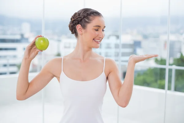 Happy sporty brunette holding green apple — Stock Photo, Image