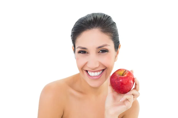 Счастливая брюнетка с красным яблоком и смотрящая в камеру — стоковое фото