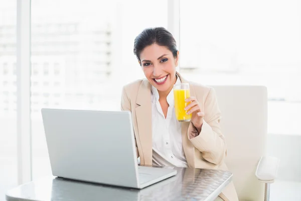 Alegre mujer de negocios con portátil y vaso de jugo de naranja en el escritorio — Foto de Stock