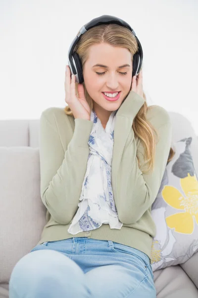 Happy cute blonde listening to music sitting on cosy sofa — Stock Photo, Image