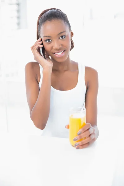 Счастливая атлетическая женщина звонит держа апельсиновый сок — стоковое фото