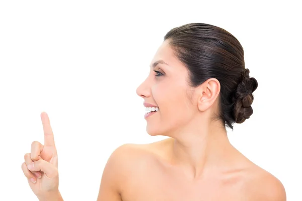 Smiling brunette pointing up with one hand with head turned — Stock Photo, Image