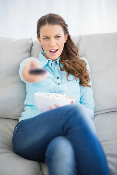 Zweifelhafte Frau sitzt auf Sofa und wechselt TV-Sender — Stockfoto