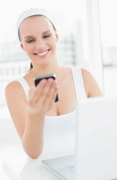 Happy pretty sportswoman looking at her mobile phone — Stock Photo, Image