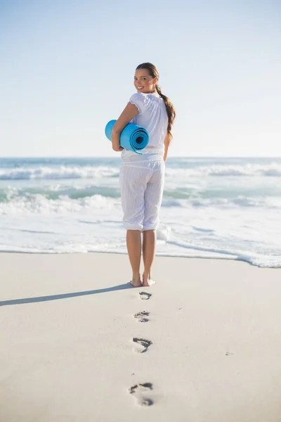 Rear view of gorgeous woman holding exercise mat looking over sh