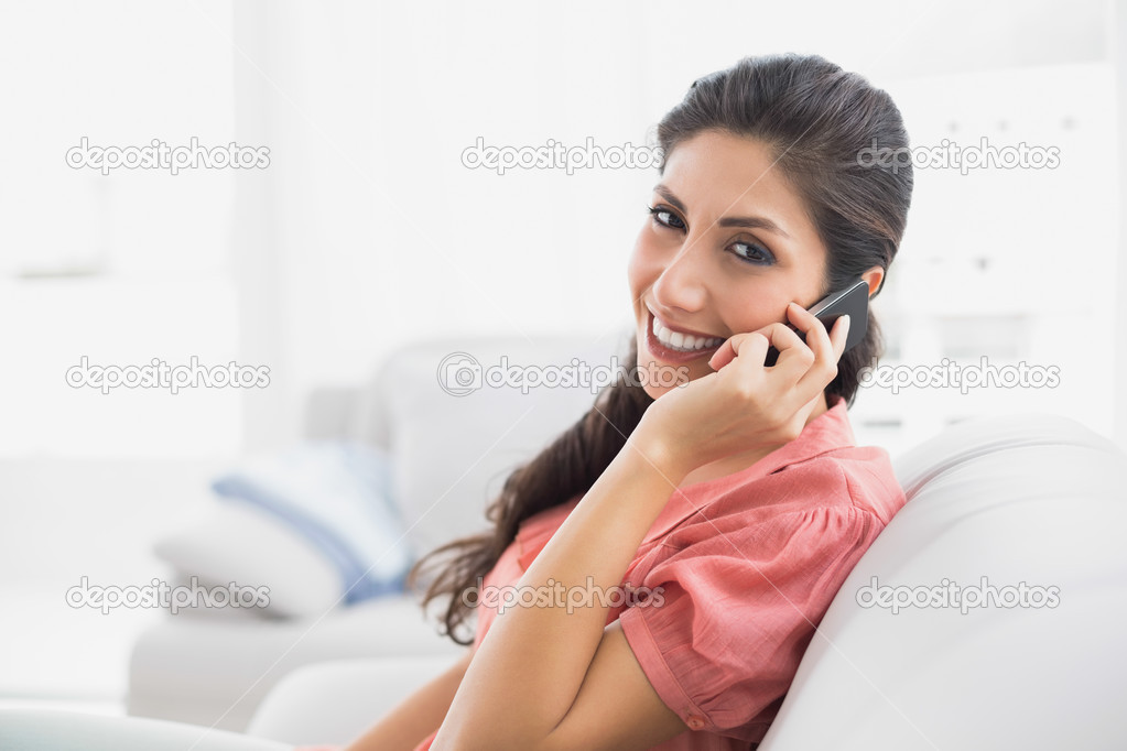 Content brunette sitting on her sofa on the phone looking at camera