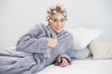 Onu yatakta yatarken saç curlers içinde mutlu rahat sarışın kadın