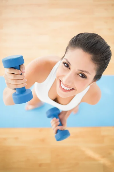 Mujer feliz haciendo ejercicio con pesas en la alfombra azul sonriendo a la cámara —  Fotos de Stock