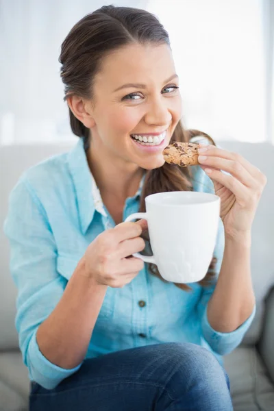Lachende vrouw eten cookie holding kopje koffie — Stockfoto