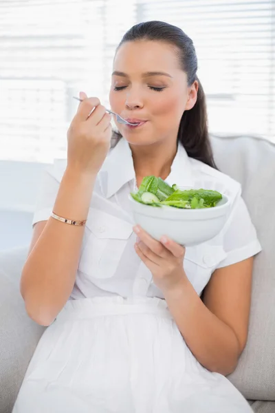 Relajada mujer bonita comiendo ensalada saludable sentado en el sofá —  Fotos de Stock