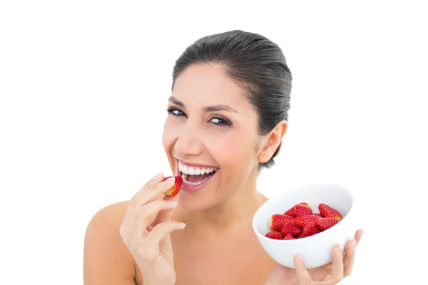 Attractive brunette holding a bowl of fresh strawberries and eating one — Stock Photo, Image