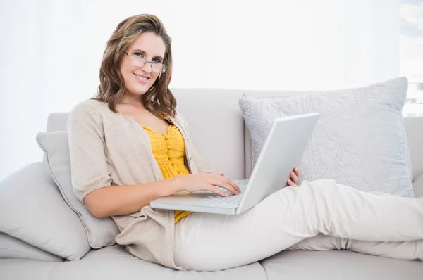 Sonriendo modelo magnífico usando el ordenador portátil en el sofá acogedor — Foto de Stock