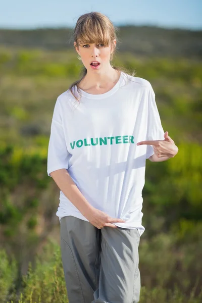 Natürliche junge Blondine zeigt auf ihr freiwilliges T-Shirt — Stockfoto