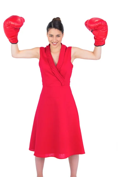 Smiling gorgeous brunette in red dress wearing boxing gloves — Stock Photo, Image