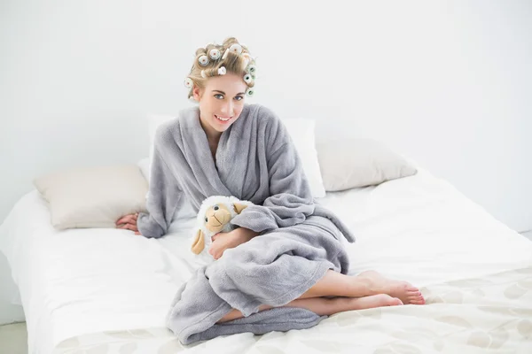 Pleased relaxed blonde woman in hair curlers cuddling a plush sheep — Stock Photo, Image