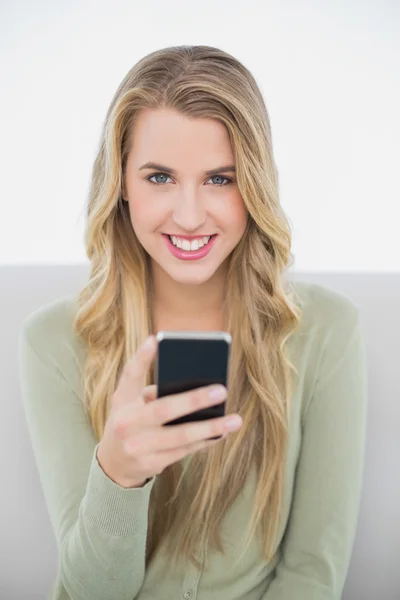 Cheerful pretty blonde sending a text sitting on cosy sofa — Stock Photo, Image