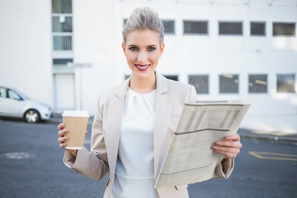 Smiling stylish businesswoman holding newspaper and coffee — Stock Photo, Image