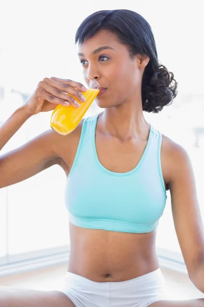 Pensive fit woman drinking a glass of orange juice — Stock Photo, Image