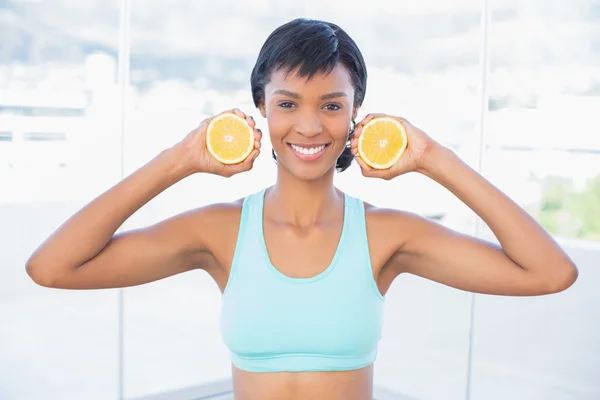 Mulher ajuste atraente segurando duas metades de uma laranja — Fotografia de Stock