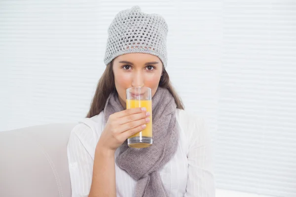 Pretty brunette with winter hat on drinking orange juice — Stock Photo, Image