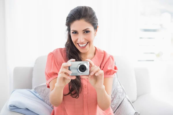 Morena feliz sentada em seu sofá tirando uma foto da câmera — Fotografia de Stock